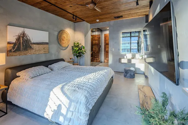 a spacious bedroom with a bed a mirror on dresser and a large window