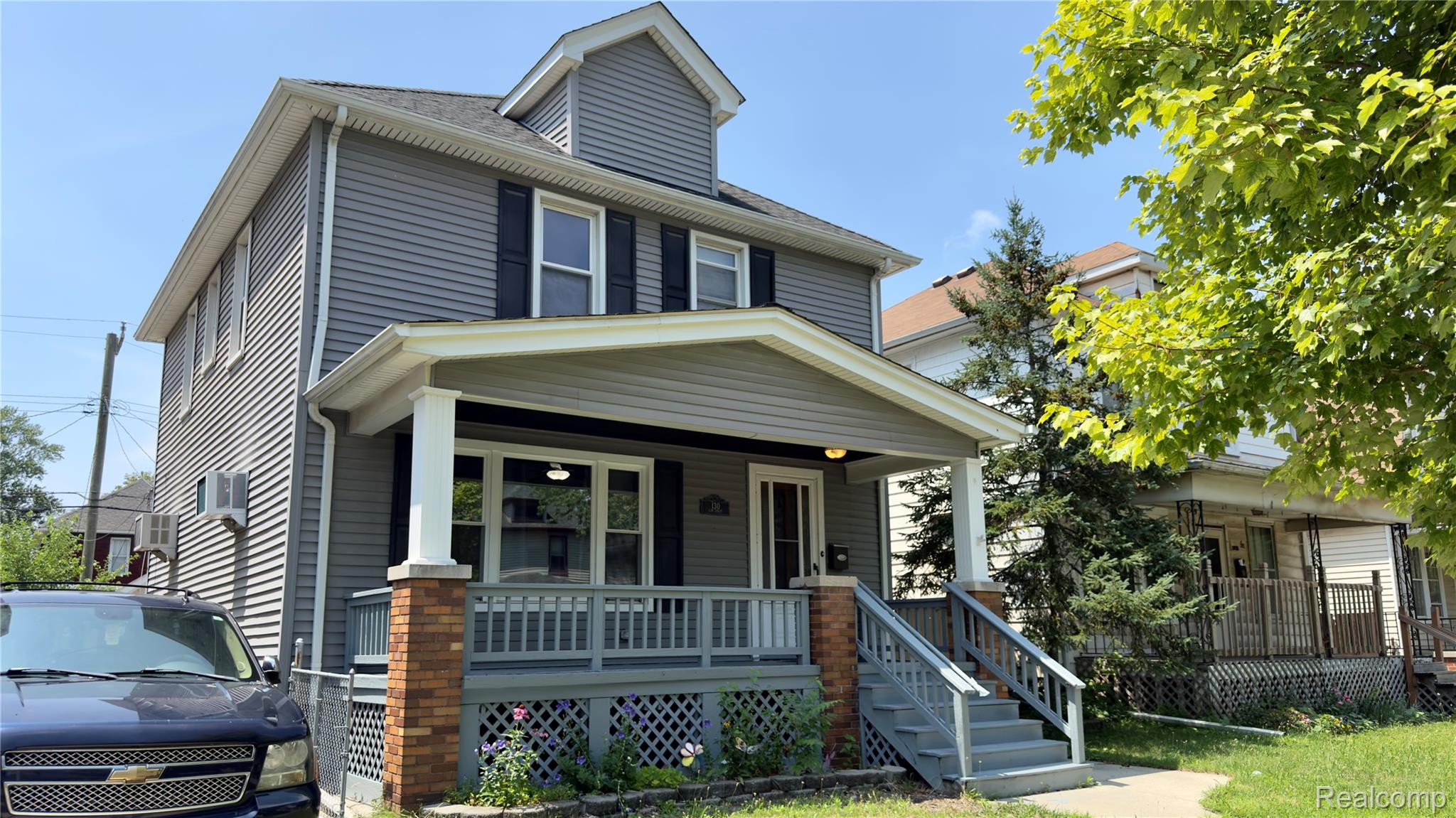 130 Elm Street River Rouge, MI 48218 - Photo 3 of 20 Two-story exterior featuring gray horizontal siding, black window shutters, a covered front porch with brick pillars, and a dormer window