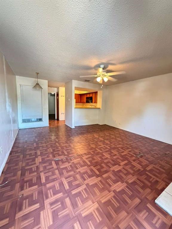 9815 Walnut Street, Unit 102 Dallas, TX 75243 - Photo 12 of 13 Open-concept living area featuring patterned wood-finish flooring, a ceiling fan with integrated lighting, and a pass-through window to the kitchen