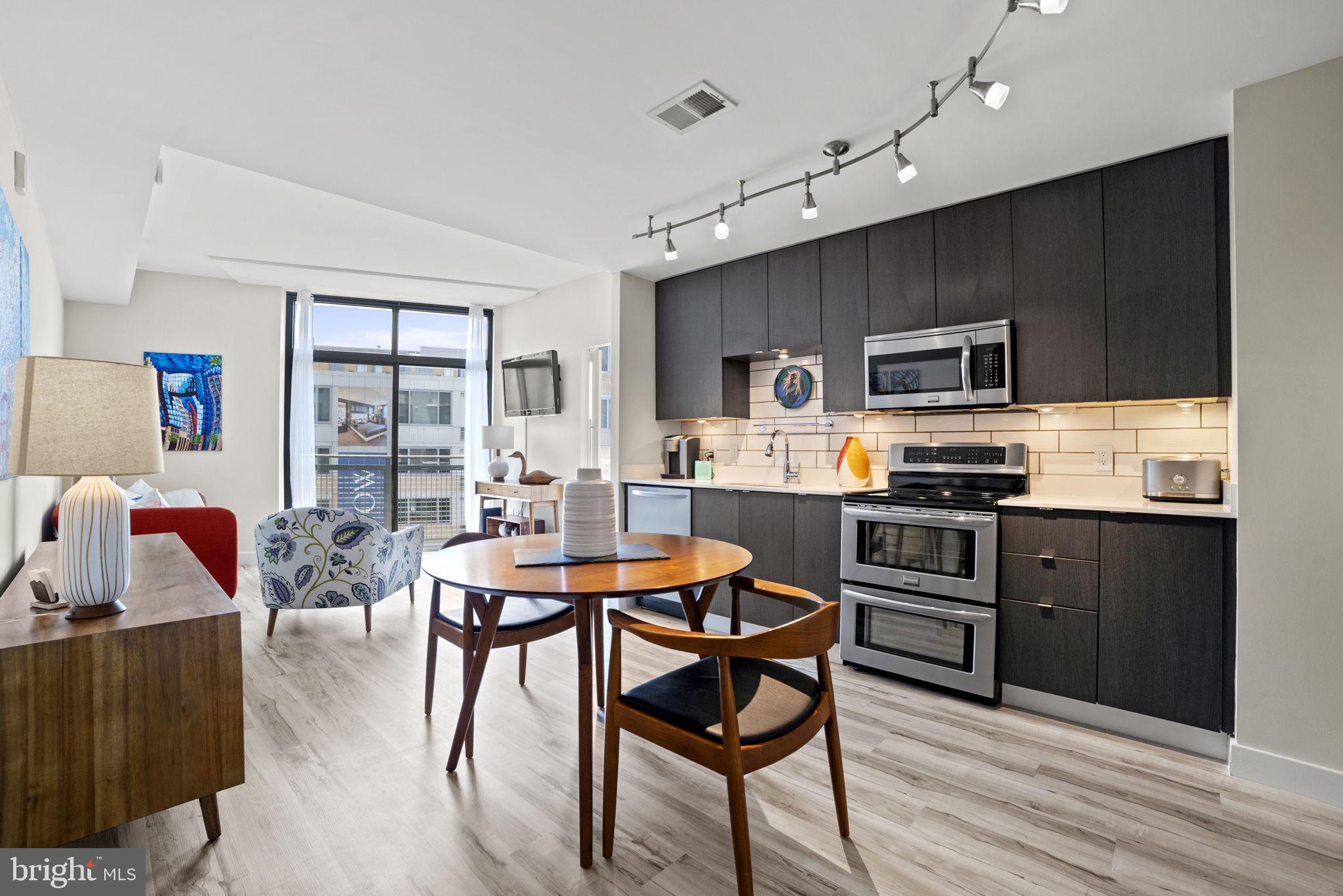 a kitchen with stainless steel appliances kitchen island granite countertop a stove a refrigerator a sink a dining table and chairs with wooden floor