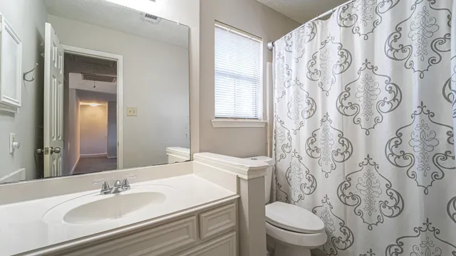a bathroom with a granite countertop toilet a sink a mirror a shower curtain and a sink