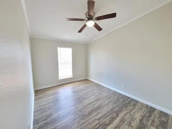 an empty room with wooden floor ceiling fan and windows