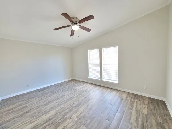 an empty room with wooden floor fan and windows