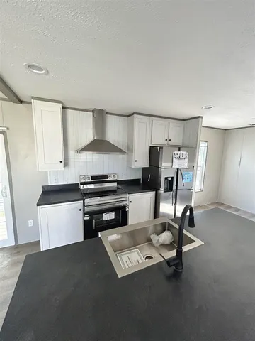 a kitchen with granite countertop a refrigerator a sink and white cabinets