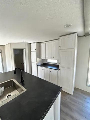 a living room with stainless steel appliances kitchen island granite countertop a sink a microwave a refrigerator and white cabinets