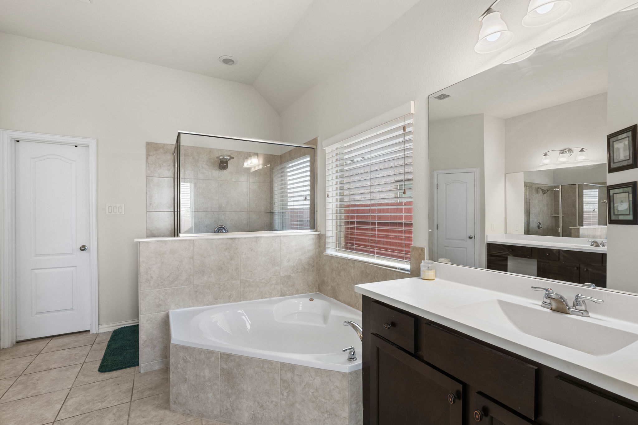 373 Rough Bark Street Buda, TX 78610 - Photo 13 of 39 A well-lit bathroom features a spacious corner soaking tub, separate shower, and a wide vanity with dual sinks.