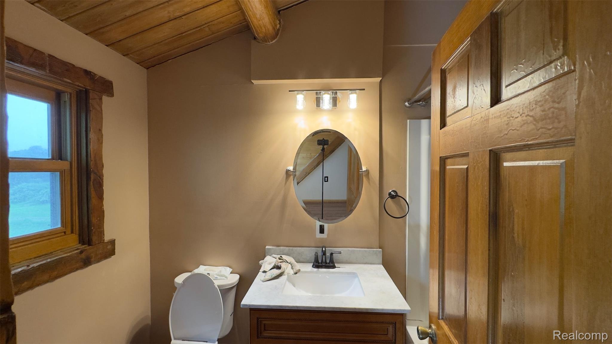 2608 East Sutton Road Metamora, MI 48455 - Photo 29 of 64 Bathroom featuring a wood-finish vanity with a white countertop and integrated sink, an oval mirror, and a three-light vanity fixture