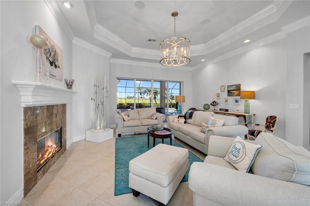 400 Terracina Way Naples, FL 34119 - Photo 7 of 29 Living room with a tray ceiling, crown molding, a tile fireplace, light tile patterned floors, and an inviting chandelier