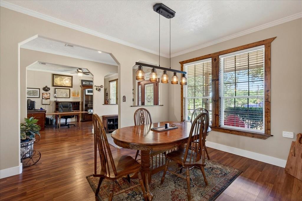 11591 Farm To Market 59 Athens, TX 75751 - Photo 10 of 40 Dining area featuring wood-finish flooring, a linear pendant light fixture with amber glass shades, and two windows framed with natural wood trim, open to living-office-kitchen.