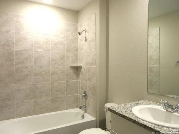 a bathroom with a granite countertop bathtub shower sink vanity and toilet