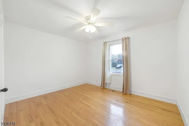 an empty room with wooden floor ceiling fan and windows