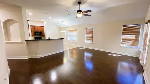 a view of an empty room with wooden floor and a kitchen