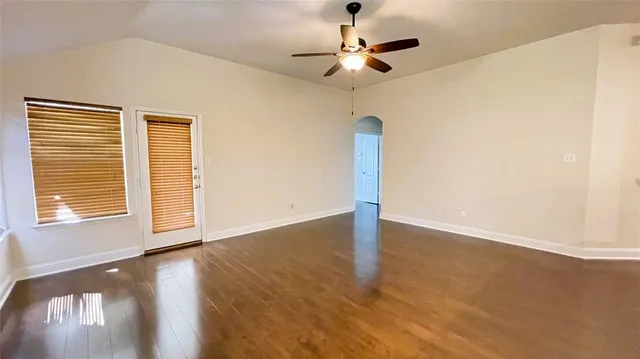 an empty room with wooden floor fan and windows