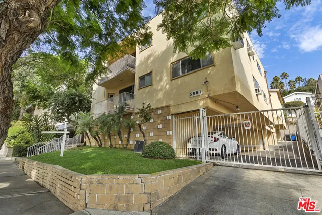 a view of a brick house with a small yard and large trees