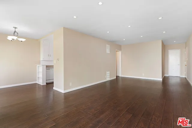 a view of an empty room with wooden floor and a kitchen