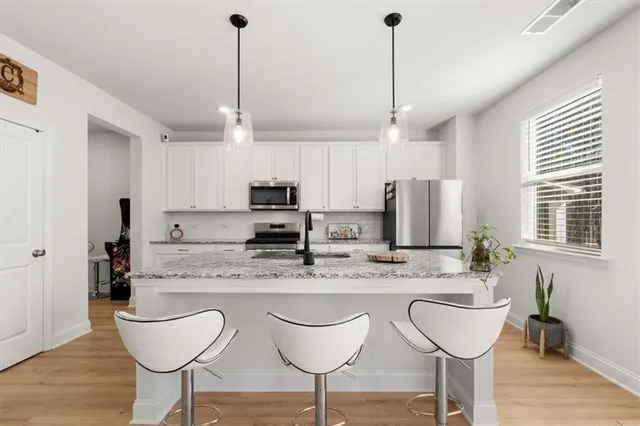a kitchen with stainless steel appliances kitchen island granite countertop a dining table chairs and white cabinets
