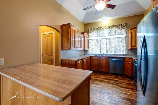 a kitchen with stainless steel appliances granite countertop a refrigerator a sink dishwasher a stove and white countertops with wooden floor