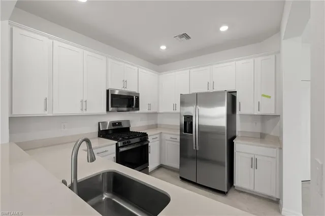 a kitchen with stainless steel appliances granite countertop a refrigerator a stove a sink and white cabinets