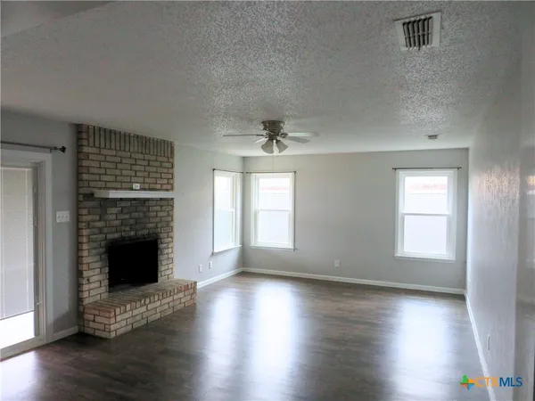 an empty room with wooden floor fireplace and windows