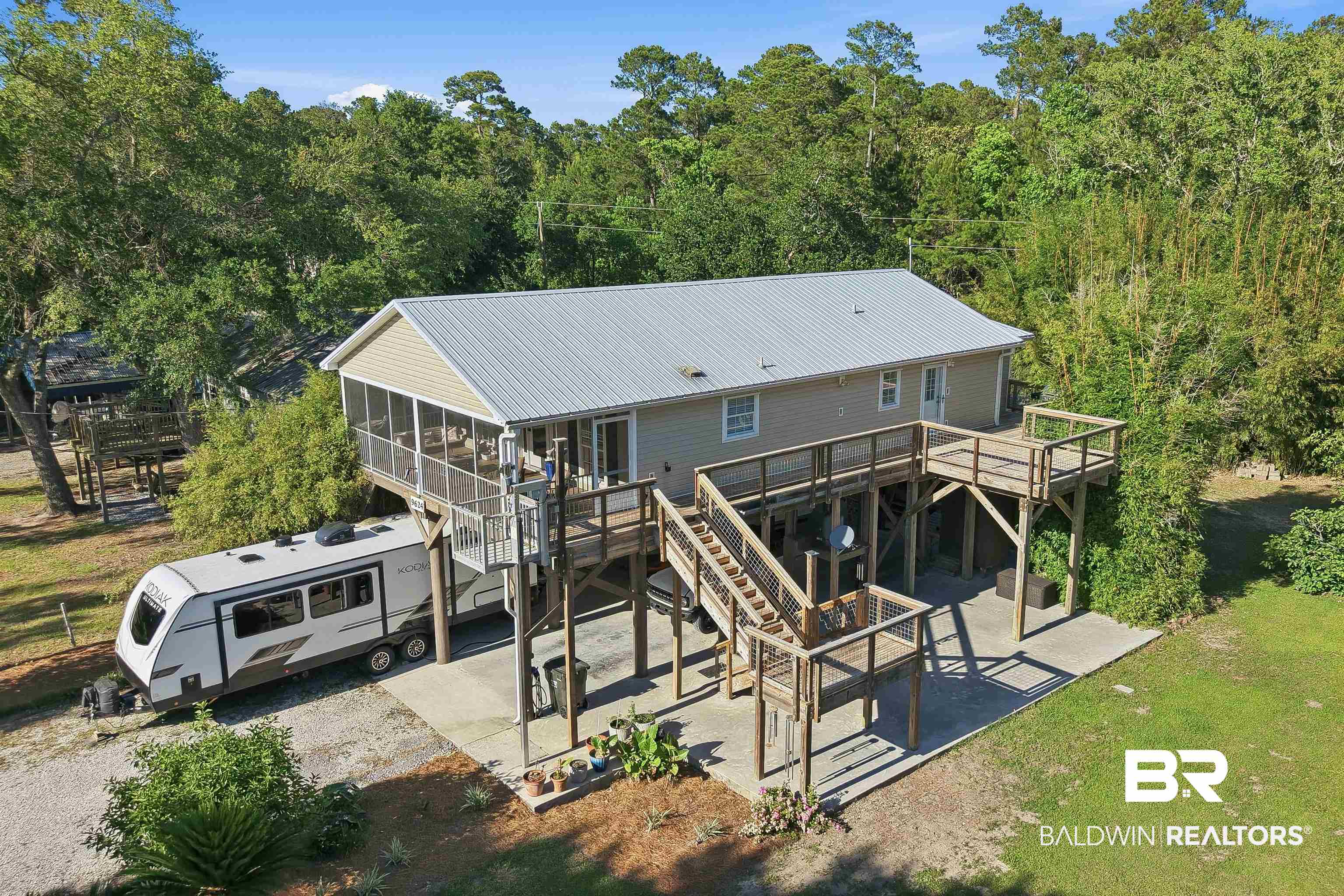 9624 North Bay Street Foley, AL 36535 - Photo 2 of 59 Elevated siding residence featuring a metal roof, expansive wraparound wooden decking, and a screened porch