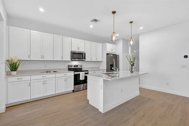 a kitchen with stainless steel appliances white cabinets a sink a stove a refrigerator and microwave