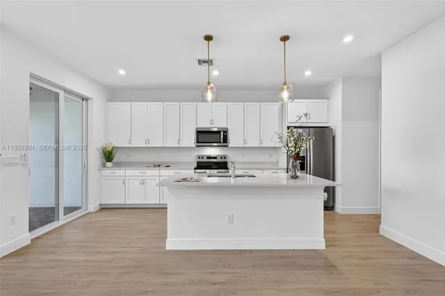 a kitchen with stainless steel appliances granite countertop a stove a sink a refrigerator and white cabinets with wooden floor