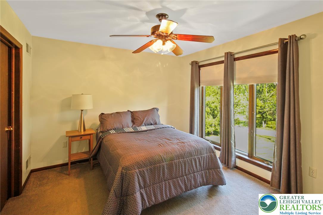 3470 Brodhead Road Bethlehem, PA 18020 - Photo 65 of 84 A quiet bedroom retreat with a warm ambiance, featuring a classic ceiling fan and large windows framing lush outdoor greenery.