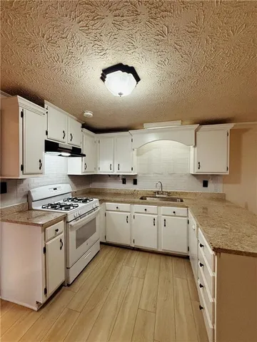 a large kitchen with granite countertop a stove top oven a sink dishwasher and white cabinets with wooden floor