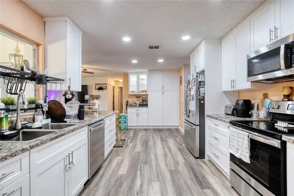 a kitchen with stainless steel appliances a stove top oven a sink a refrigerator white cabinets and wooden floor