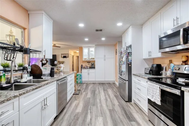 a kitchen with stainless steel appliances a stove top oven a sink a refrigerator white cabinets and wooden floor