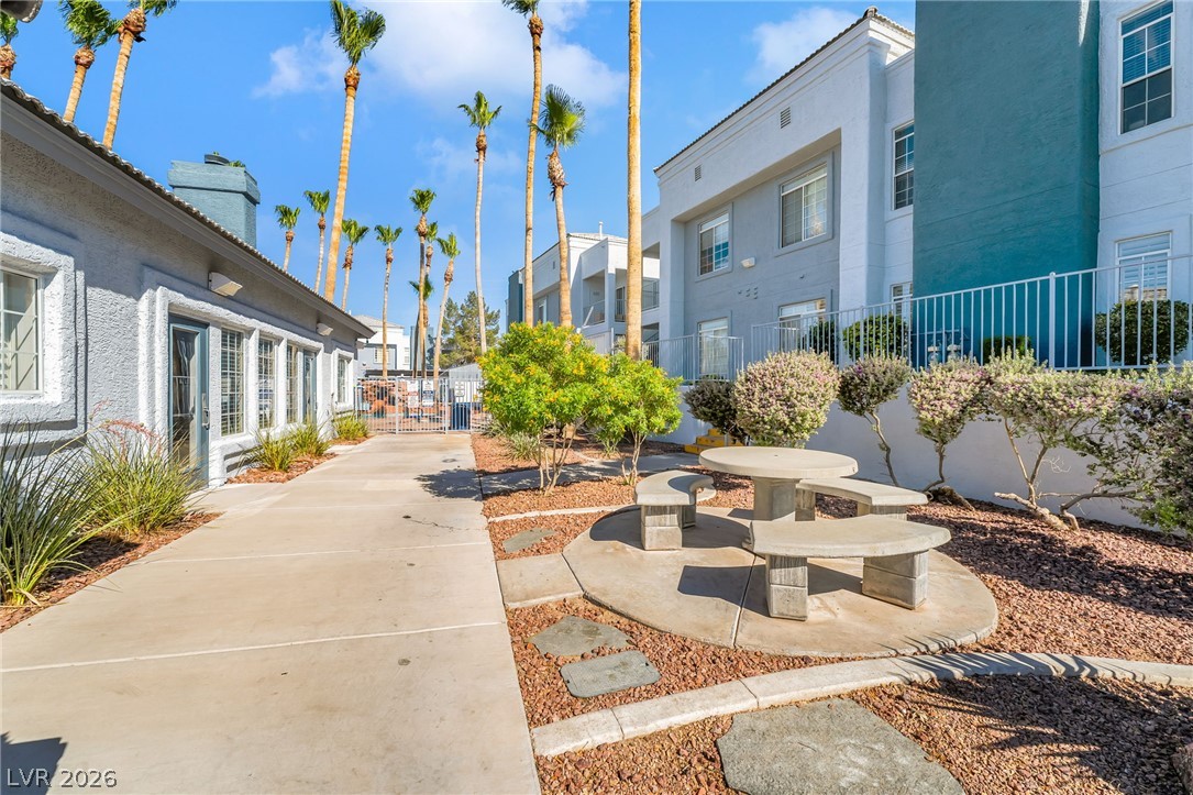 2201 Ramsgate Drive, Unit 811 Henderson, NV 89074 - Photo 33 of 36 Concrete pathways wind through lush landscaping, offering a pleasant outdoor gathering area with a built-in stone picnic table.