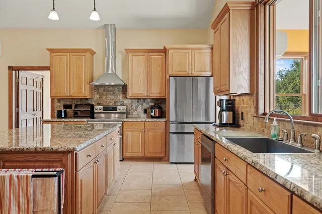 a kitchen with kitchen island granite countertop a sink a counter top space stainless steel appliances cabinets and a large window