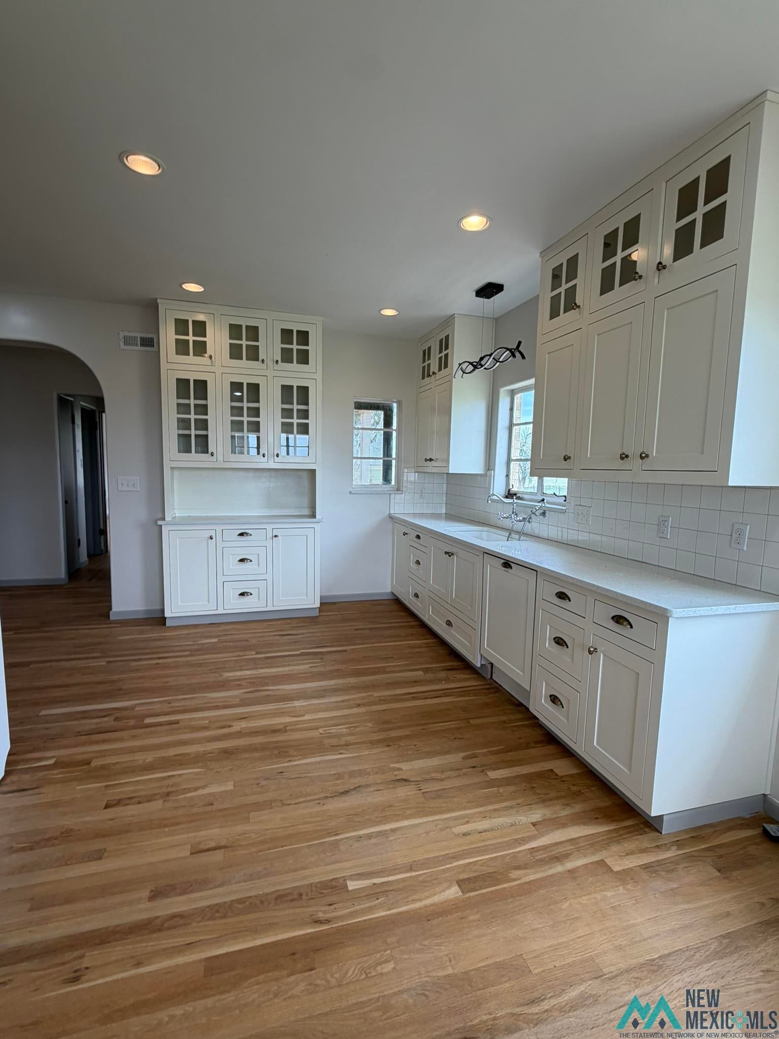 570 Curry Road North Clovis, NM 88101 - Photo 8 of 59 Open-concept kitchen featuring extensive white cabinetry with glass-front uppers, light-toned wood-finish flooring, recessed ceiling lighting, and a subway tile backsplash