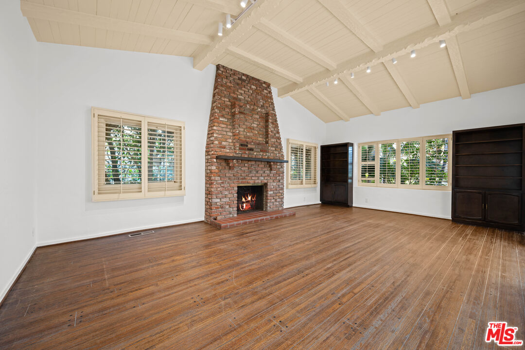 an empty room with wooden floor fireplace and windows