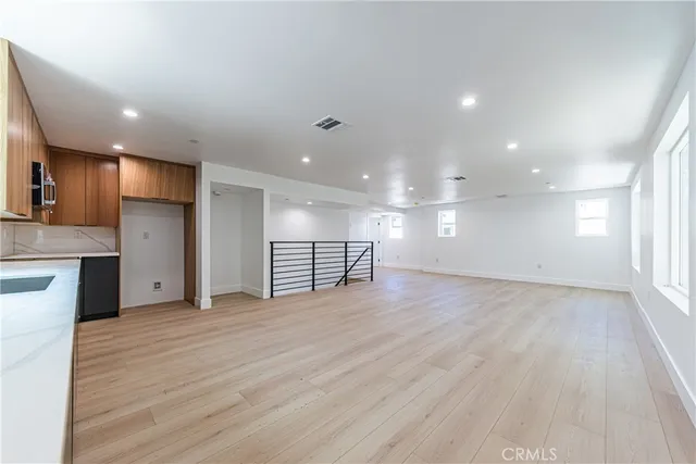 a view of an empty room with wooden floor and a kitchen
