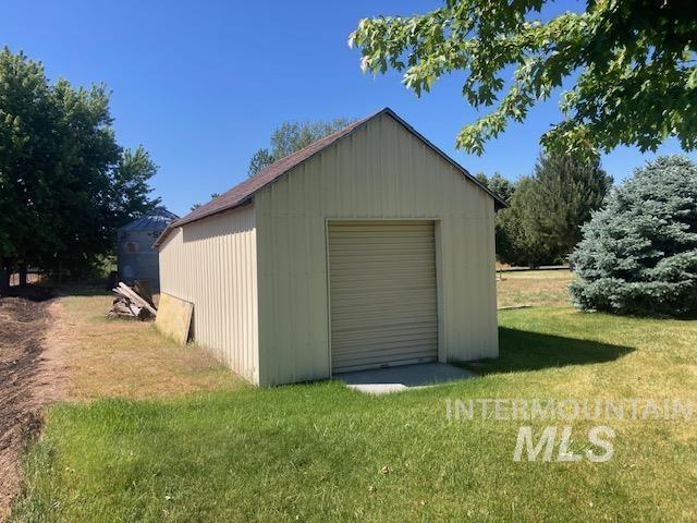 1095 County Road 70 Weiser, ID 83672 - Photo 35 of 44 Detached outbuilding with a roll-up door, corrugated siding, and an asphalt shingle roof, set on a concrete pad amidst a grassy area