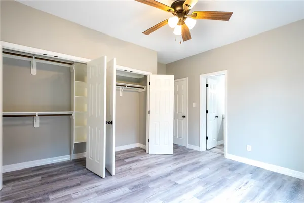 an empty room with wooden floor closet fan and windows