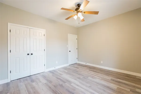 an empty room with wooden floor chandelier fan and windows