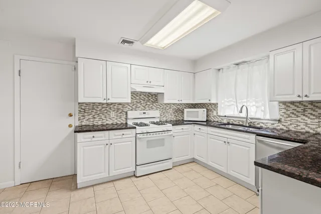 a kitchen with granite countertop white cabinets sink and white appliances