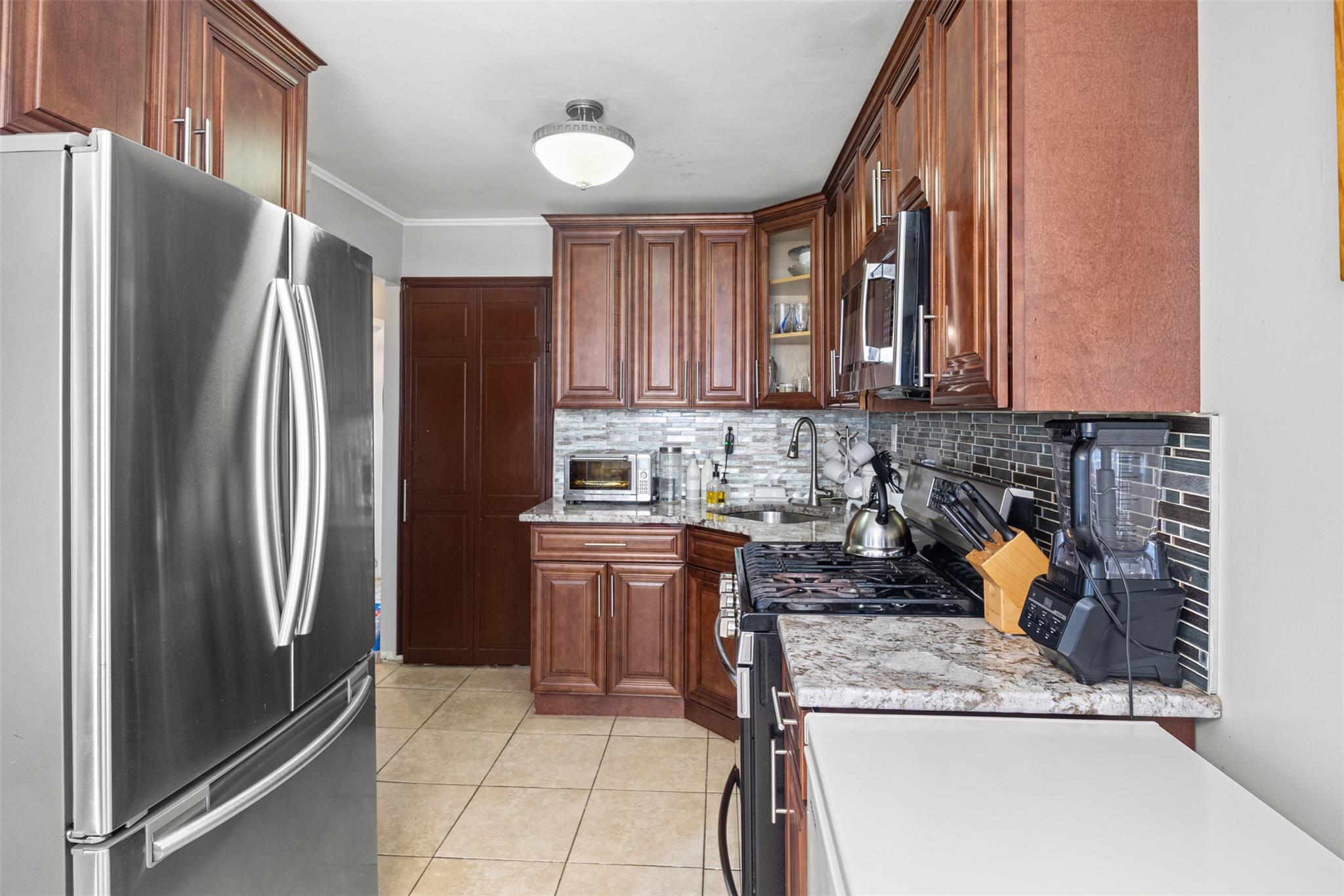 239-15 147th Road Queens, NY 11422 - Photo 2 of 28 Kitchen with appliances with stainless steel finishes, light tile patterned flooring, tasteful backsplash, crown molding, and light stone countertops