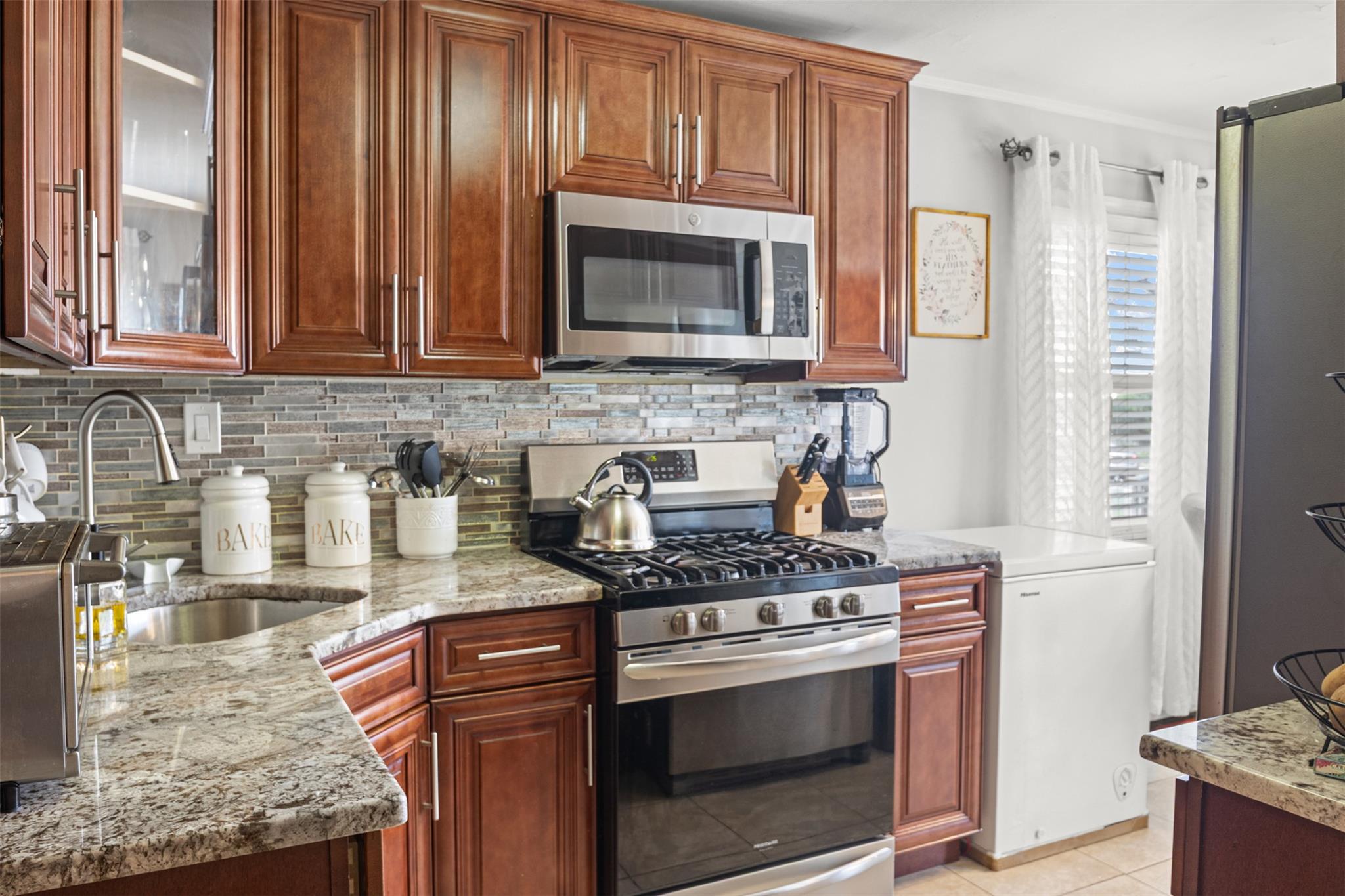 239-15 147th Road Queens, NY 11422 - Photo 6 of 28 Kitchen with appliances with stainless steel finishes, light stone countertops, ornamental molding, tasteful backsplash, and glass insert cabinets