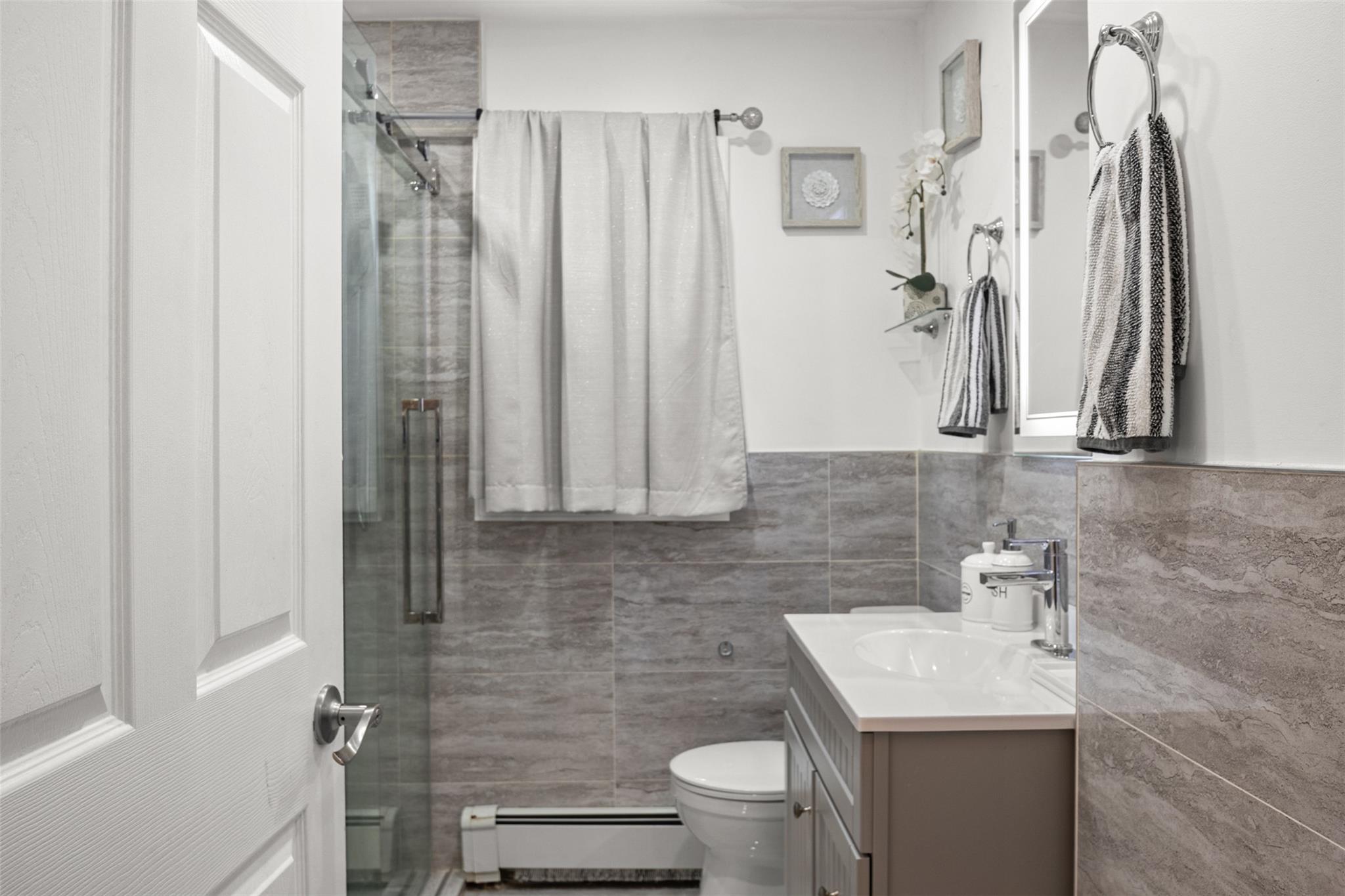 239-15 147th Road Queens, NY 11422 - Photo 7 of 28 Bathroom with tile walls, vanity, a baseboard heating unit, and a stall shower