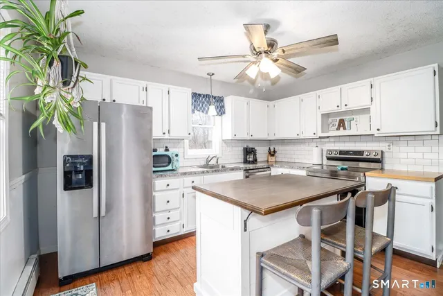 a kitchen with stainless steel appliances a white refrigerator a sink a stove a dining table and chairs