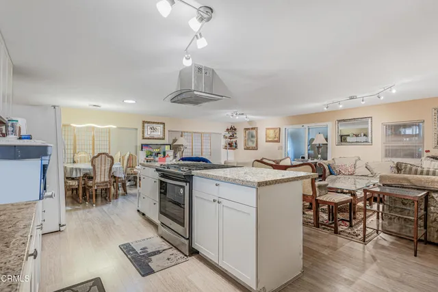 a open kitchen with stainless steel appliances granite countertop a stove top oven a dining table and chairs with wooden floor