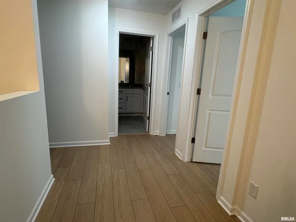 a view of a hallway with wooden floor and a bathroom