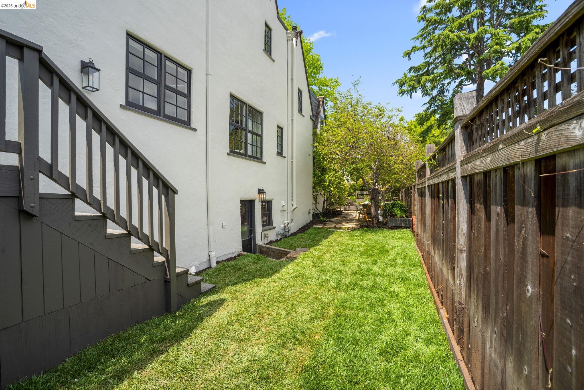 1087 Hubert Road Oakland, CA 94610 - Photo 57 of 67 Manicured lawn area bordered by a privacy fence and a white stucco exterior with dark-trimmed windows
