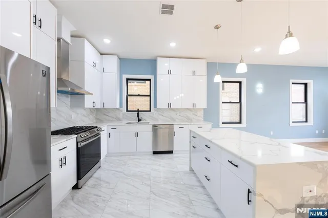 a large white kitchen with granite countertop a sink a stove a refrigerator and a stove top oven with white cabinets