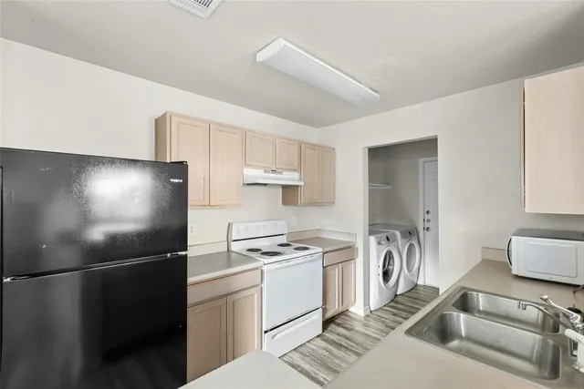 a kitchen that has a refrigerator a stove and white cabinets with wooden floor