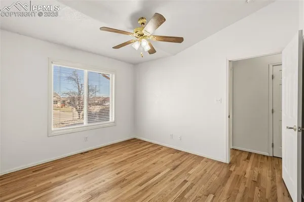 an empty room with wooden floor chandelier fan and windows