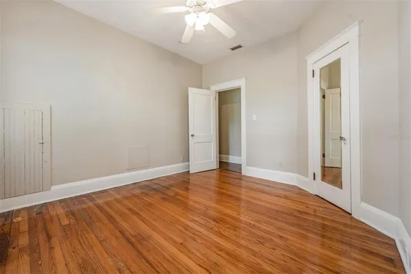 a view of an empty room with wooden floor and a ceiling fan